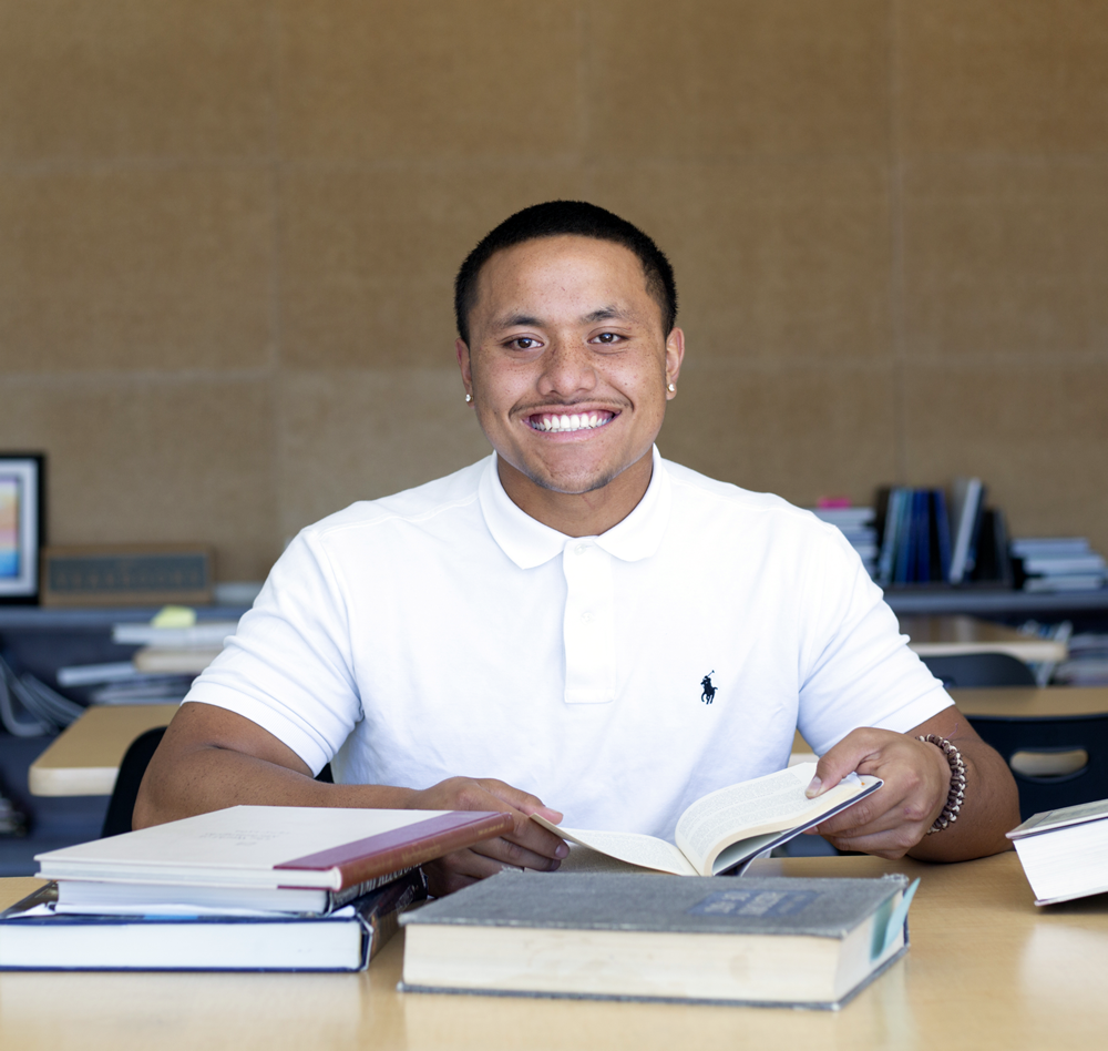 student smiles at a table with books