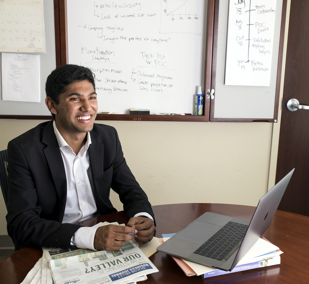 student in suit sits in front of a laptop and newspapers